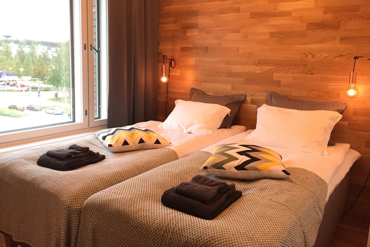 A hotel room with two beds, a large window, wooden wall paneling, and a view of the outside.
