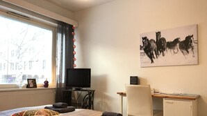 Makuuhuoneessa on sänky, työpöytä, tuoli, televisio ja maalaus, jossa on kuvattuna hevosia.