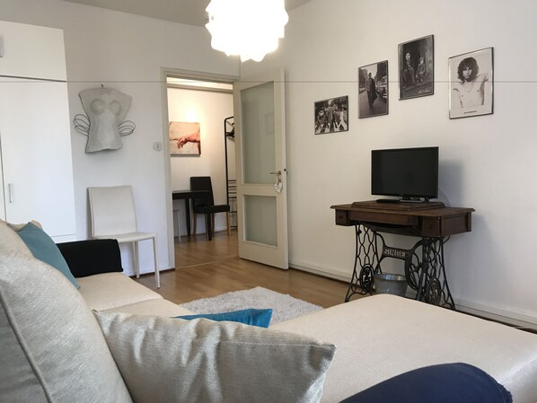 A living room with a sofa, a television on a wooden table, and a door leading to another room.