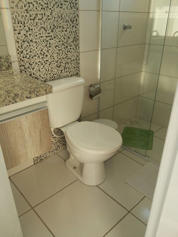 Un baño con inodoro, ducha y piso de baldosas.