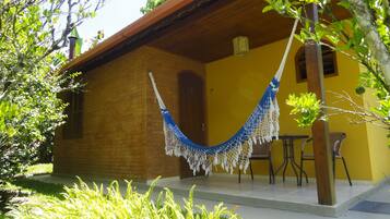 A yellow building with a hammock hanging from a tree, a patio with chairs, and a brick wall.