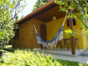 A yellow building with a hammock hanging from a tree, a patio with chairs, and a brick wall. - Pousada Chácara do Rio (Nova Friburgo)