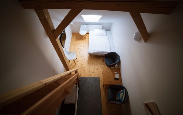 A compact room with a bed, a chair, a small table, and a skylight.