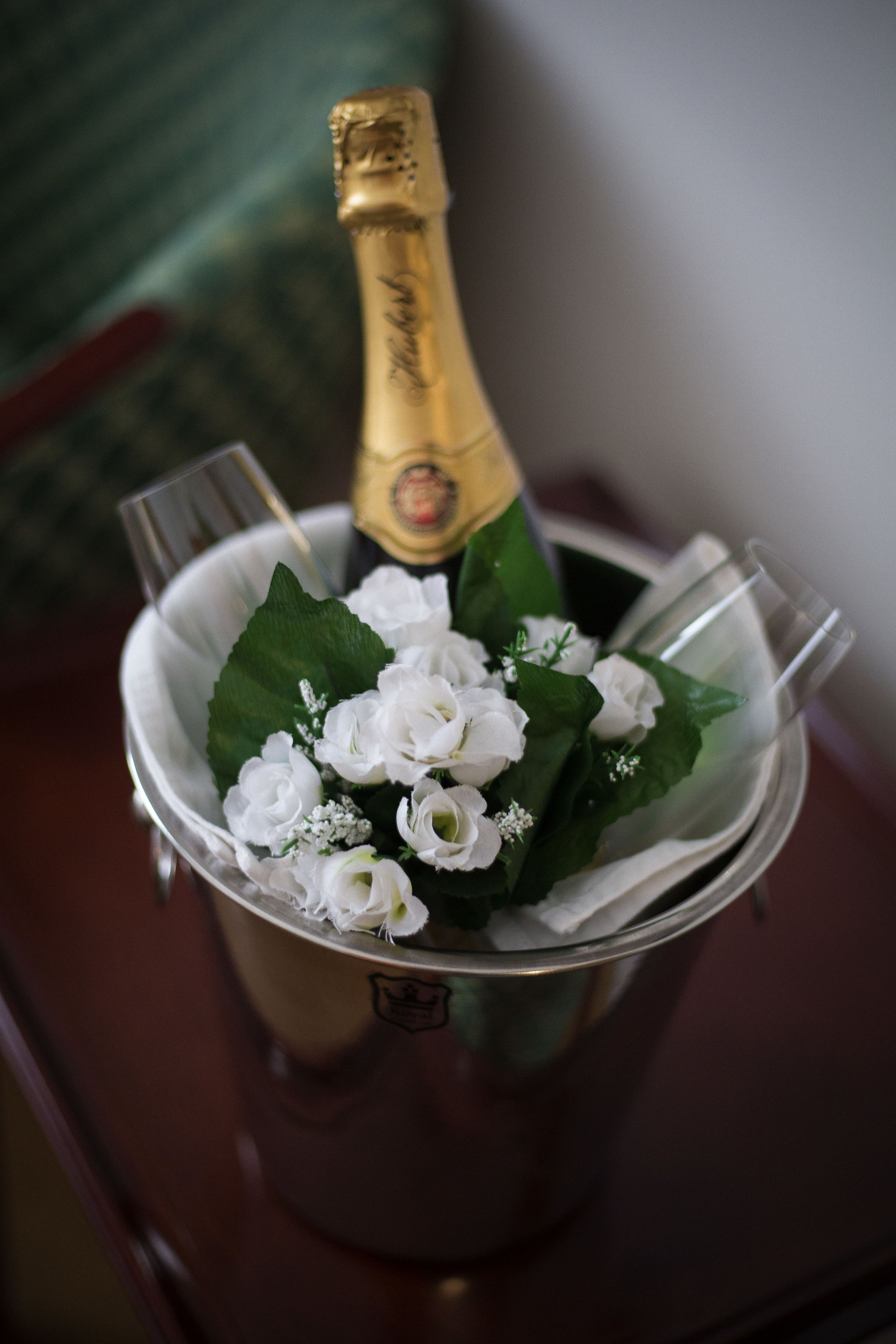 A bucket containing a bottle of champagne, glasses, and white flowers.