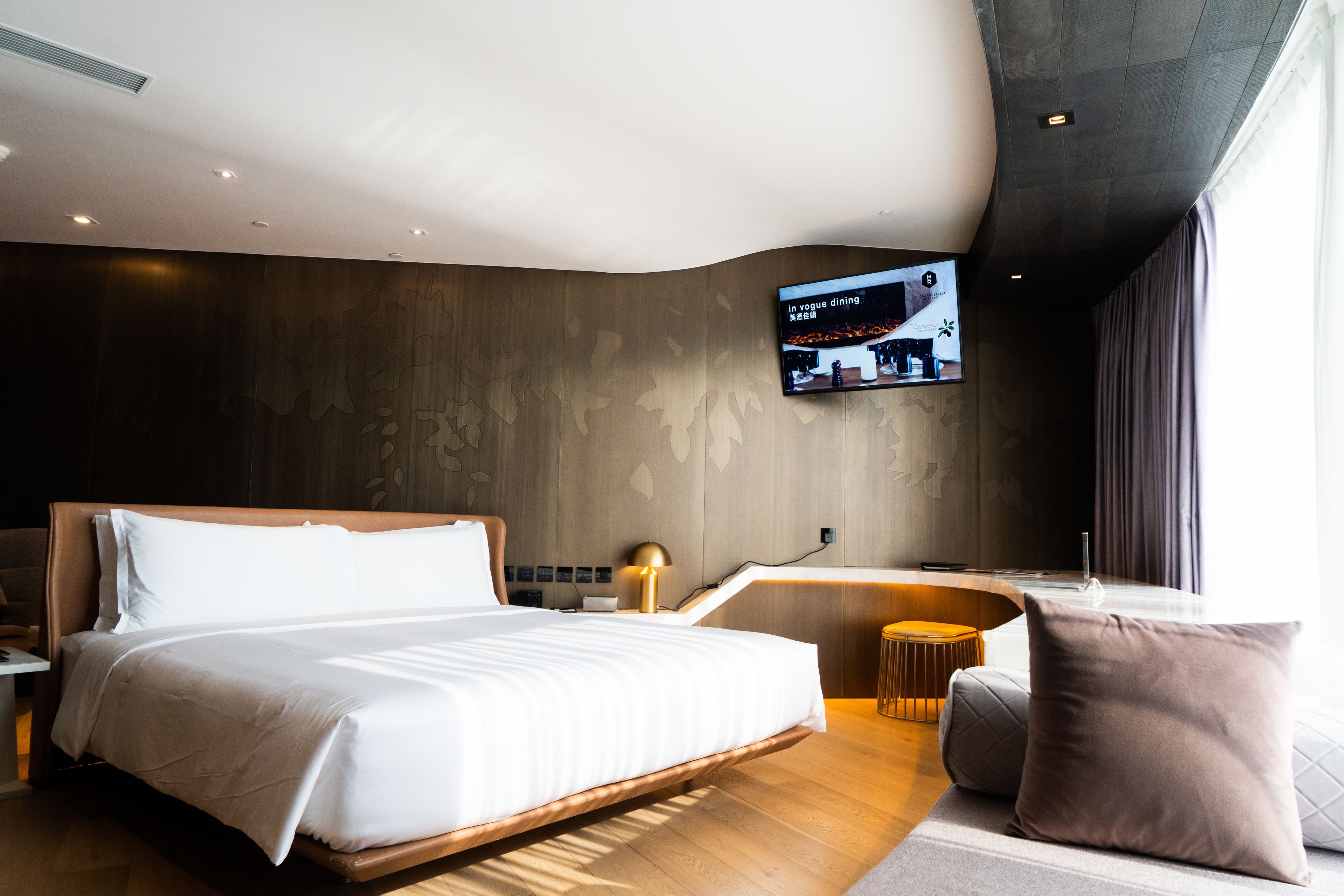 A modern hotel room with a large bed, a desk, a flat-screen TV, and a view of the city.