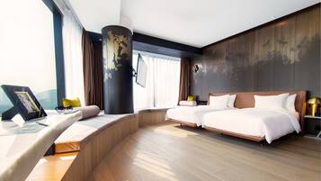 Habitación de hotel moderna con un escritorio curvo, dos camas, un ventanal grande y vista a la ciudad.