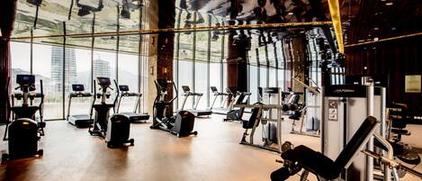 A gym with cardio machines, weight equipment, and large windows offering city views.