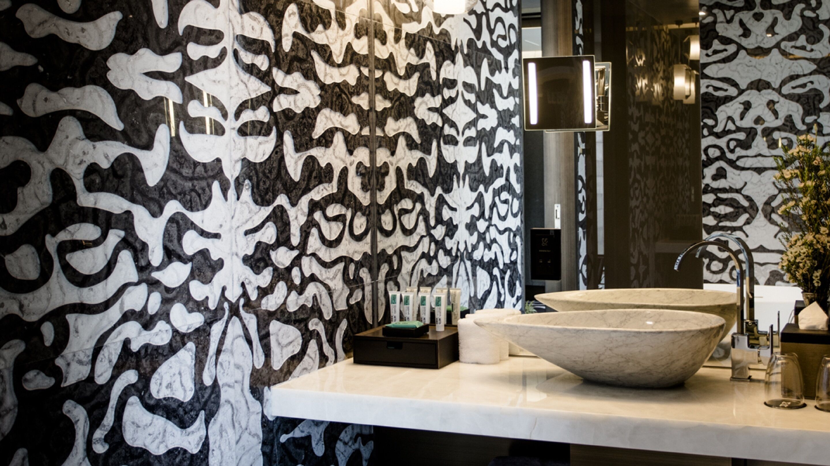 A bathroom with a large marble sink, a mirror, and a patterned wall.