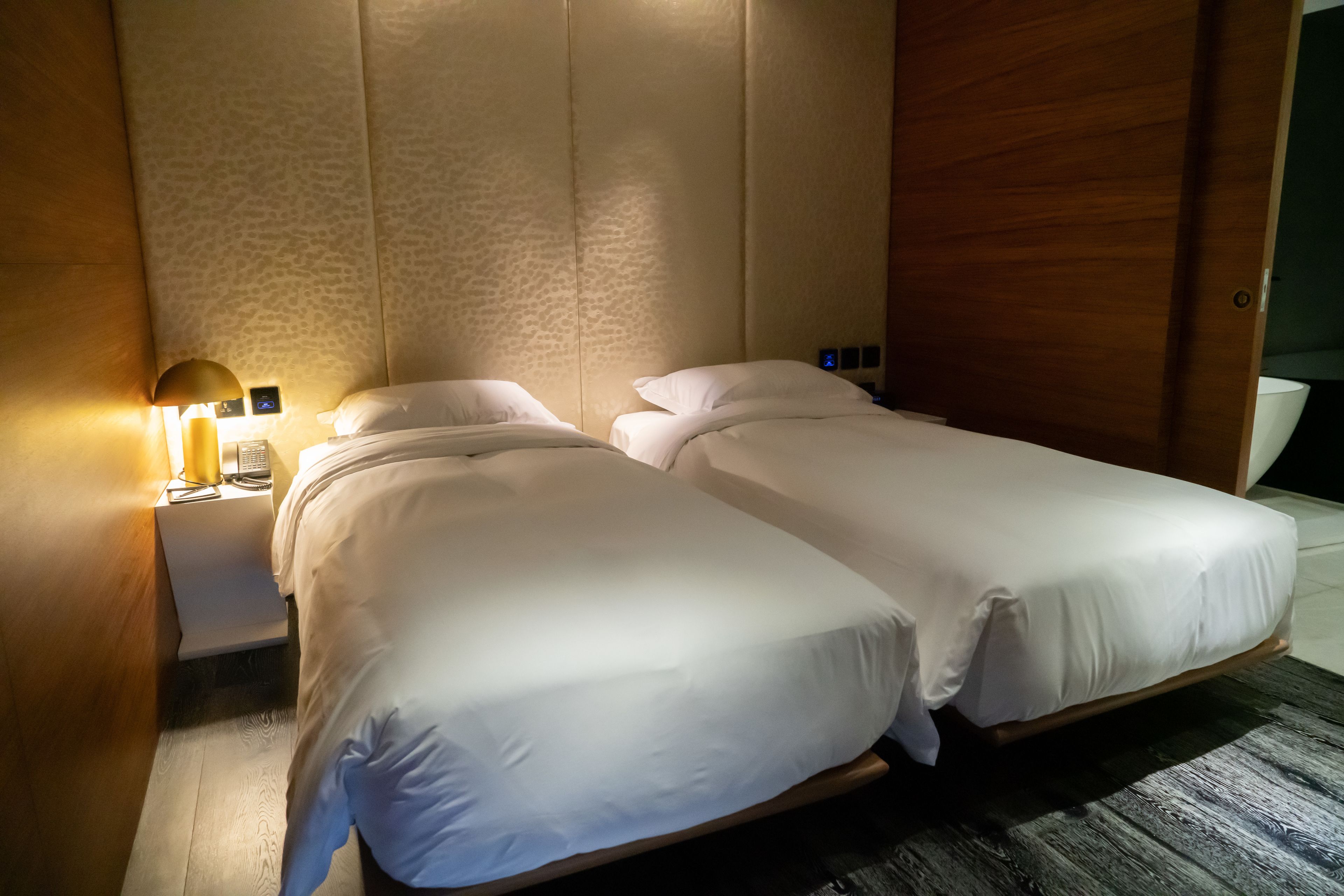 Une chambre d’hôtel avec deux lits simples, une table de chevet avec une lampe et une armoire en bois.