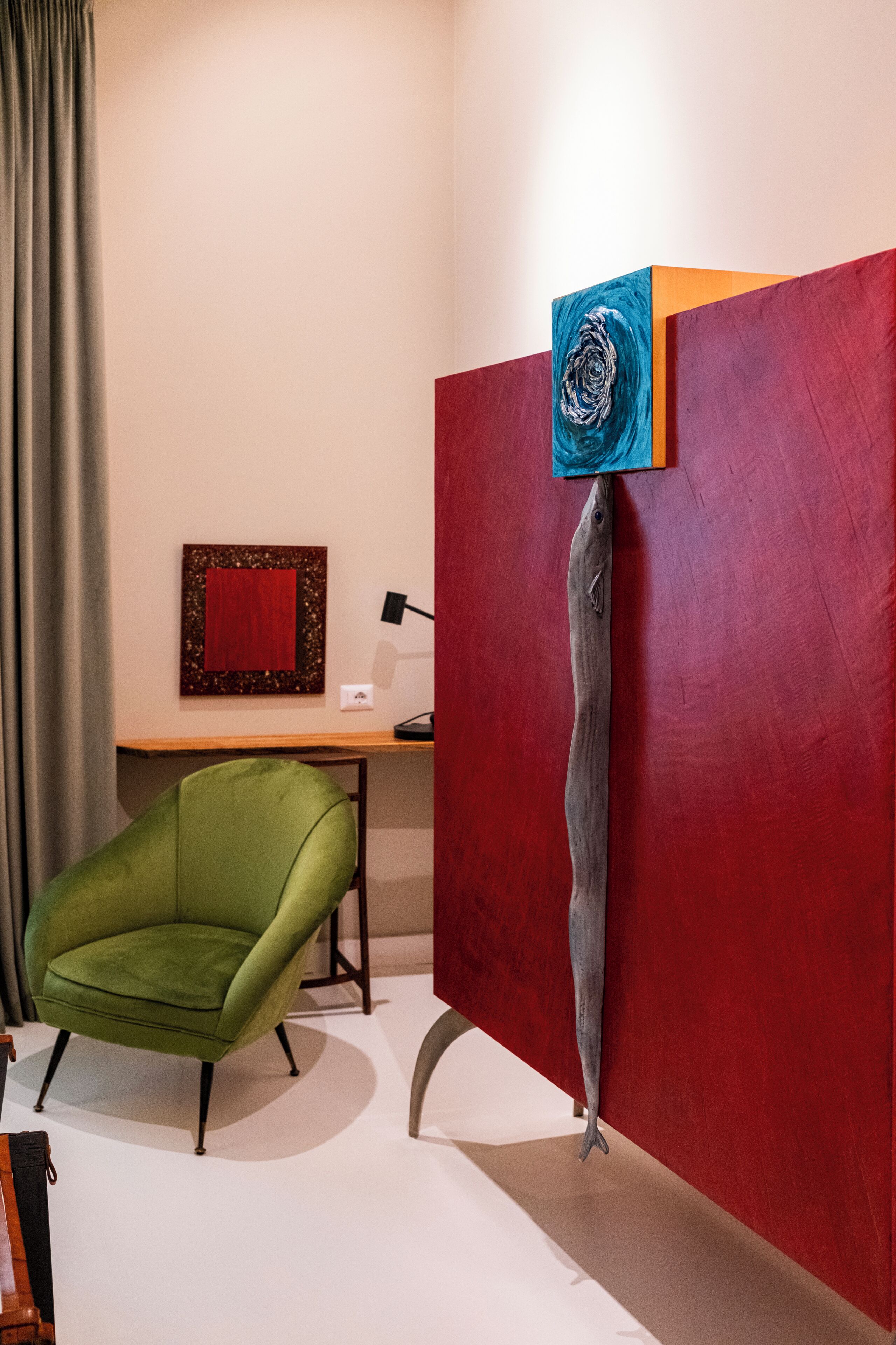 A room with a green armchair, a red partition, and a painting on the wall.