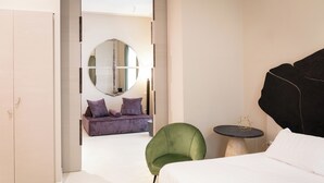 A modern bedroom with a bed, a green armchair, a round mirror, and a purple sofa.