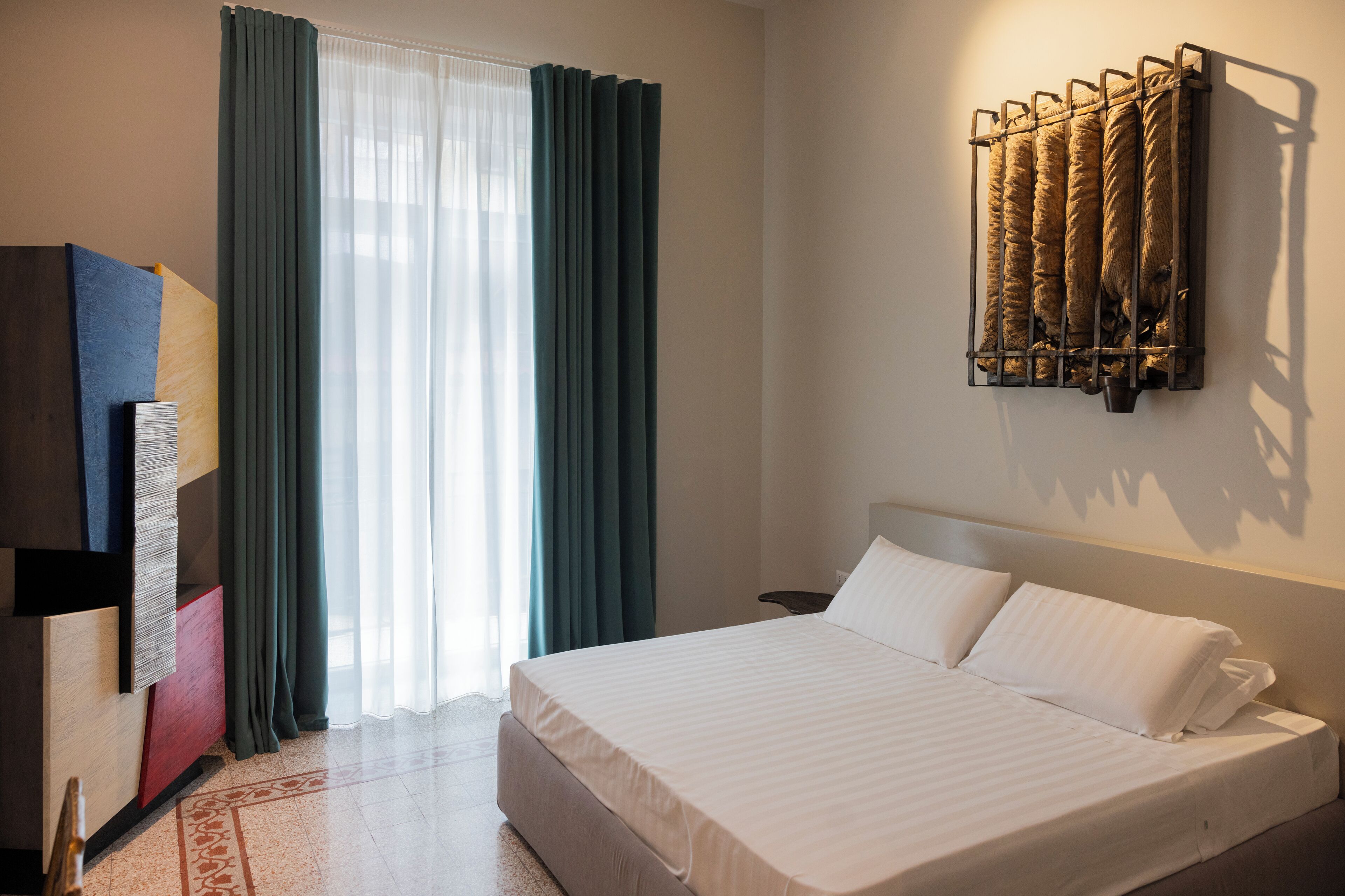 Ein Hotelzimmer mit Bett, Wandradiator, Schreibtisch mit Stuhl und einem Fenster mit Vorhängen.