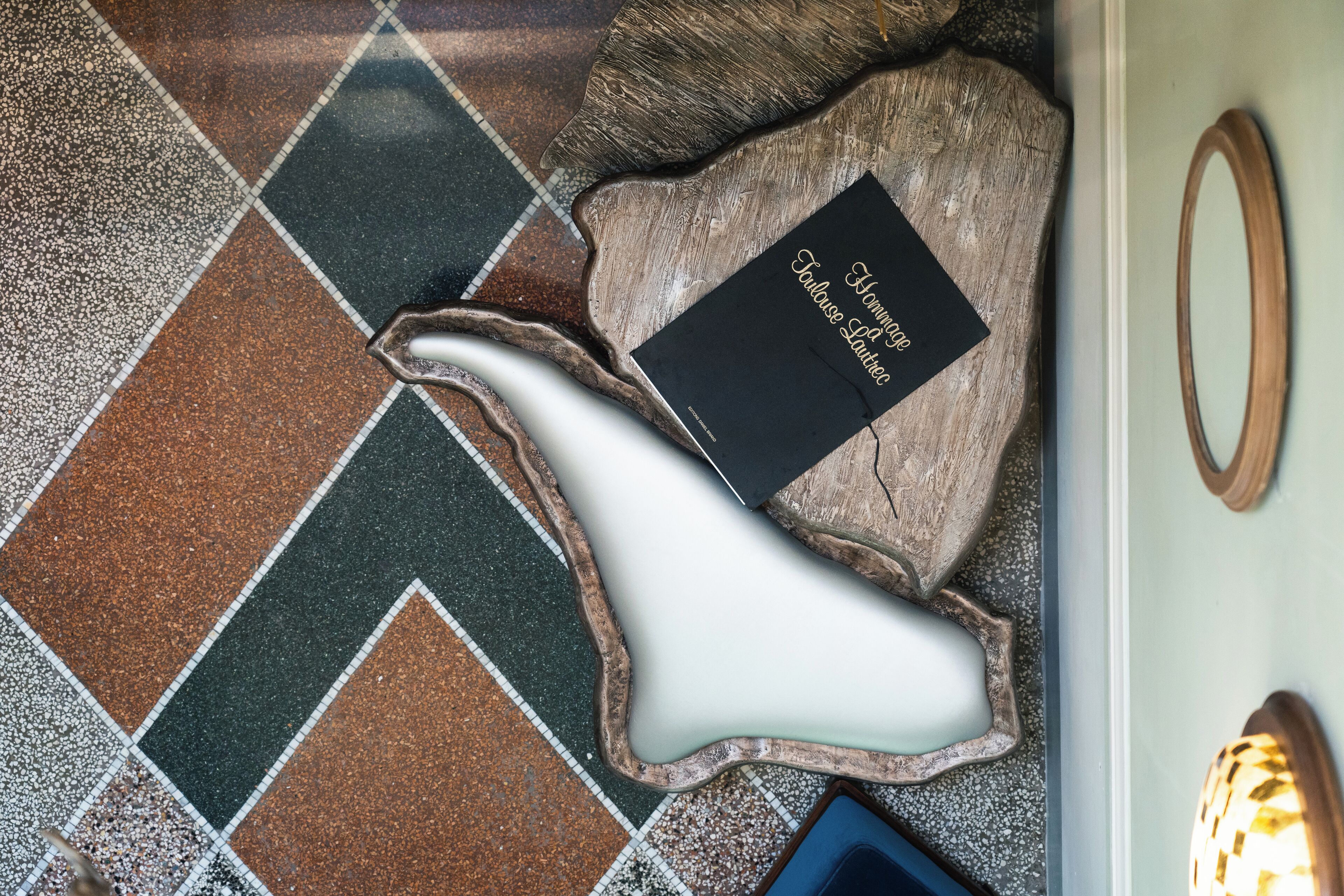 A tiled floor with a unique, irregularly shaped white object and a black plaque with gold lettering.