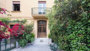 A courtyard with a wooden door, steps leading to a balcony, and a bench.
