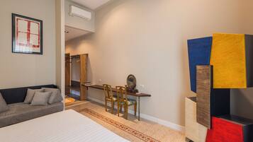 A modern hotel room with a bed, a sofa, a desk with chairs, and a colorful abstract art piece.