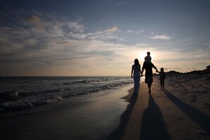 A beach scene with a sunset, featuring a family walking along the shore.