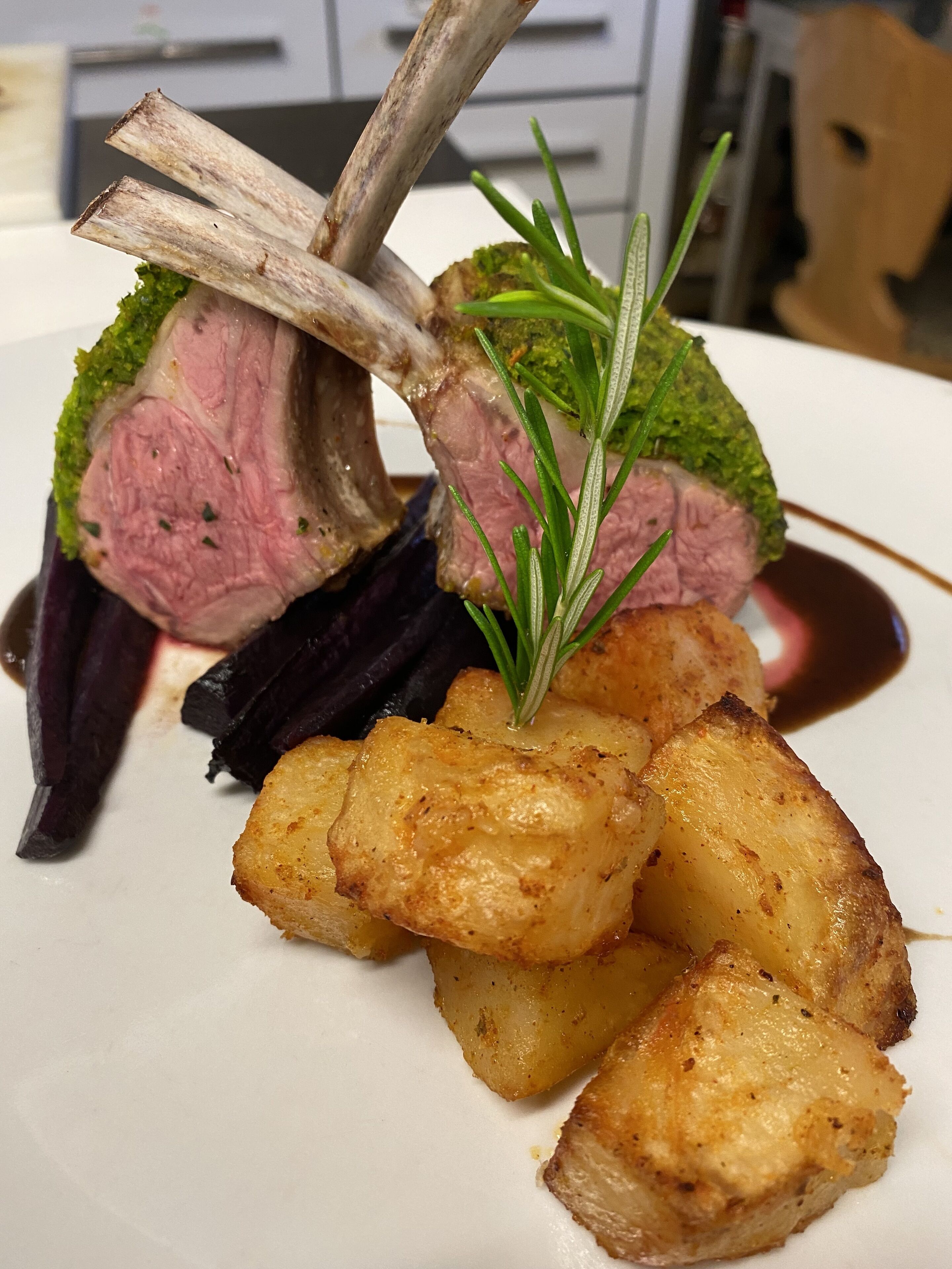 A plate of food with roasted potatoes, a lamb chop, and a green garnish.