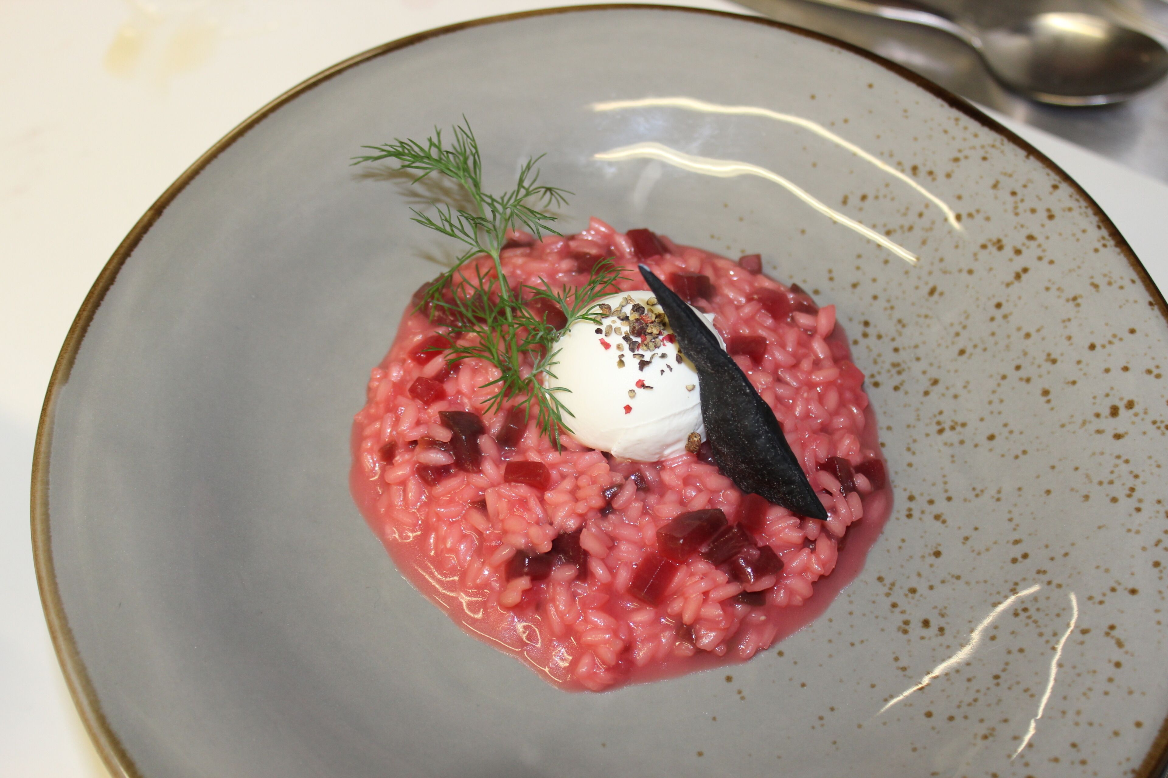 A plate of food with a dollop of cream, a sprig of dill, and a black garnish.