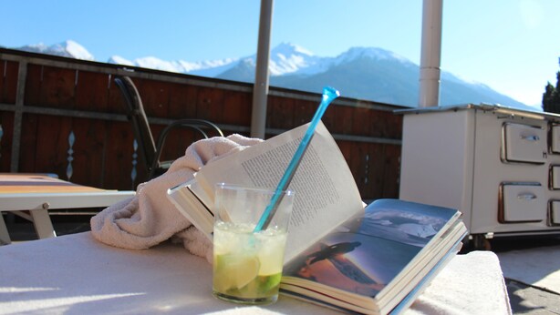 A table with a drink, a book, and a towel, with a mountain view in the background. - Pension Widmann (Moso in Passiria)