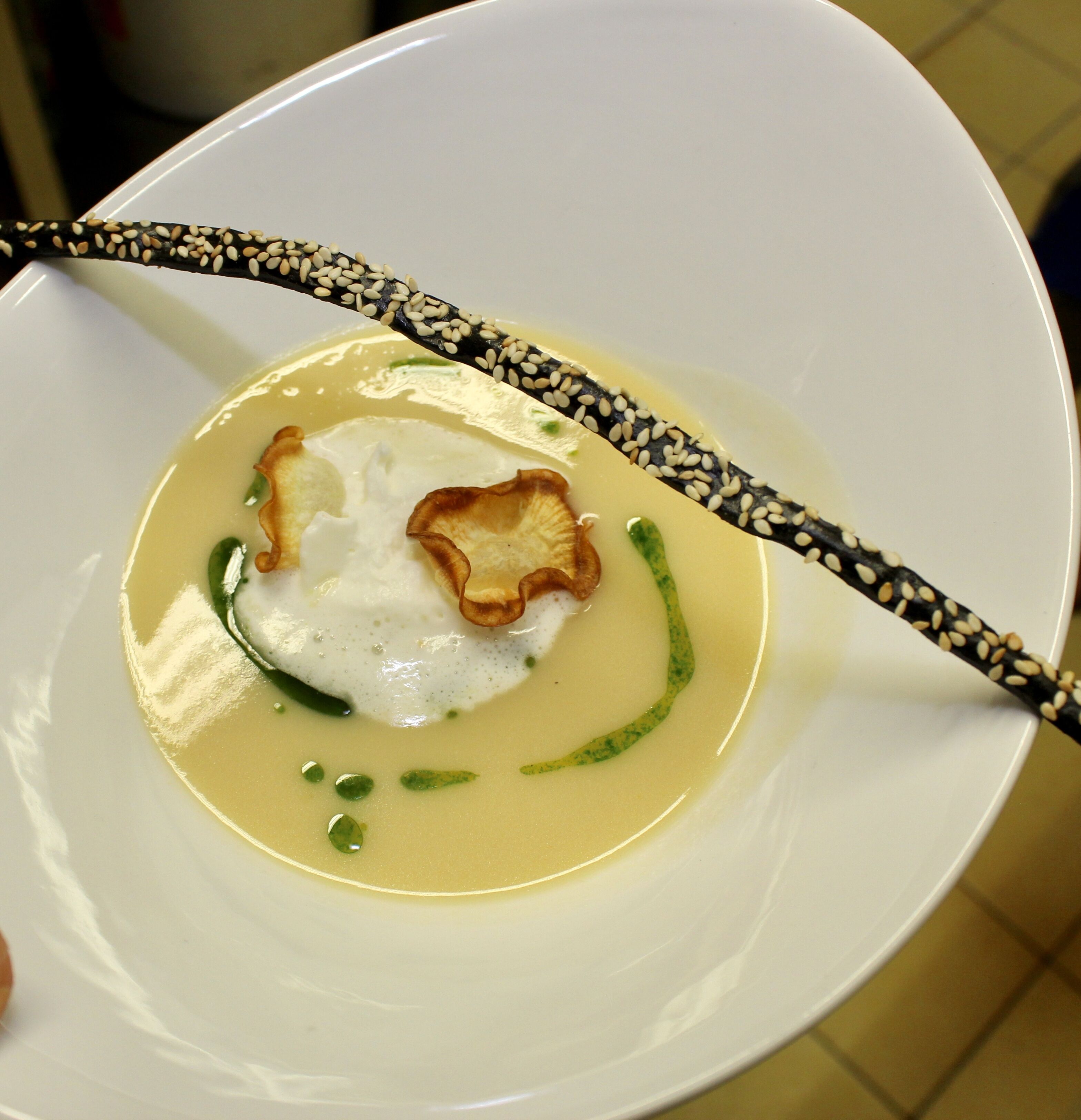 A white plate with a soup, green garnish, and a piece of fried food.