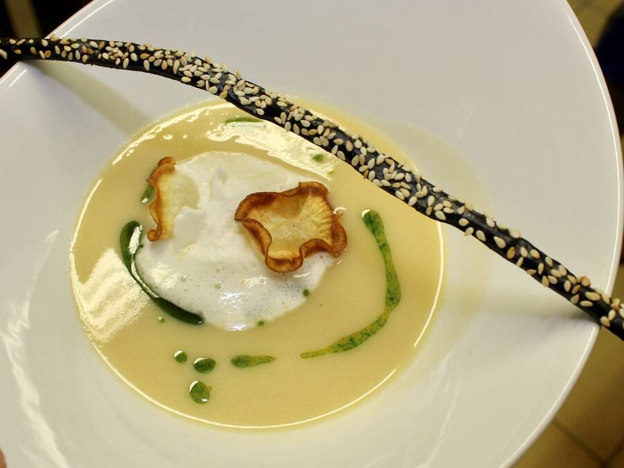 Un plato blanco con sopa, guarnición verde y un trozo de comida frita.