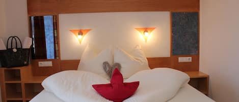 A hotel room with a wooden headboard, two bedside lamps, a bed with white bedding, a red pillow, and a nightstand with a black bag.