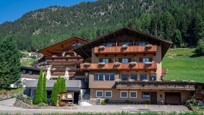 A multi-story wooden building with balconies, a restaurant and cafe, and a parking area. - Pension Widmann (Moso in Passiria)