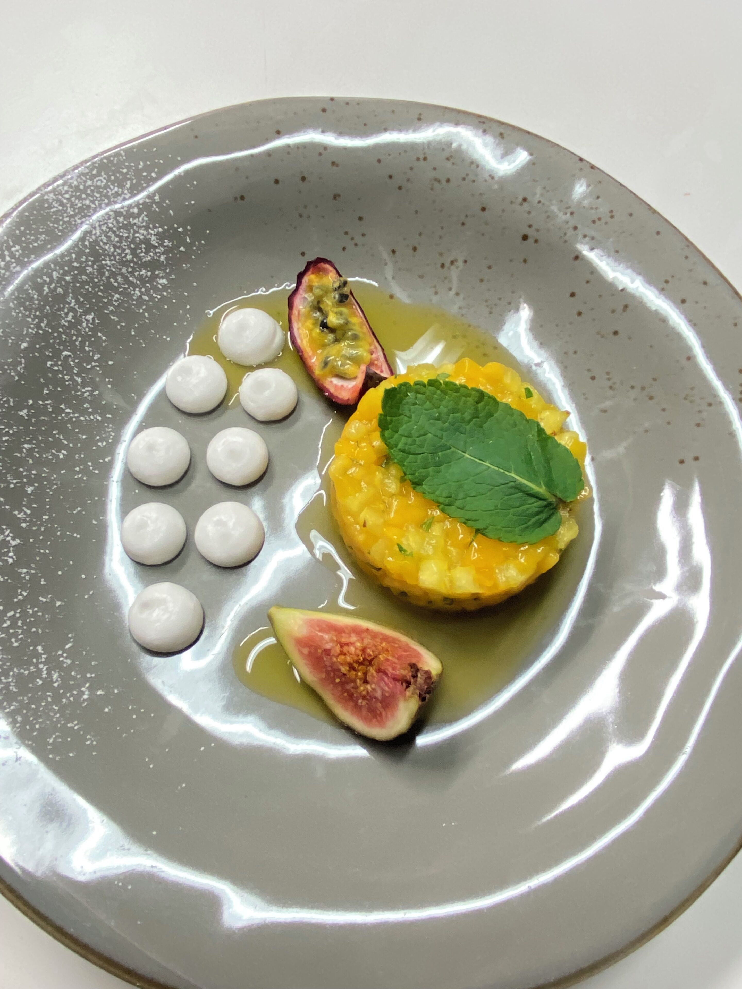 A plate with a yellow fruit, a green leaf, and a halved fruit on a gray plate.