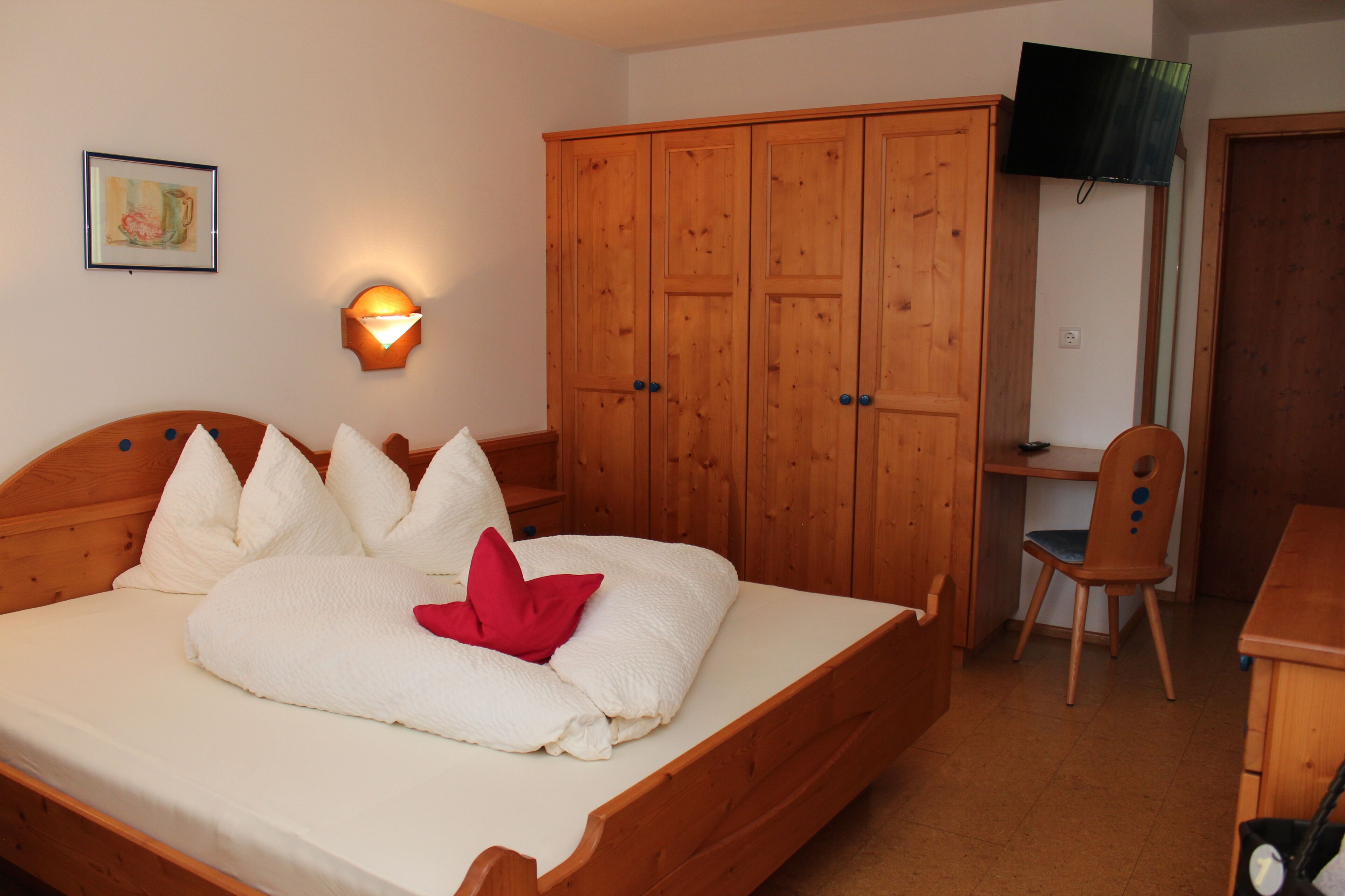 Un dormitorio con una cama de madera, un armario, un escritorio con silla y un televisor en la pared.