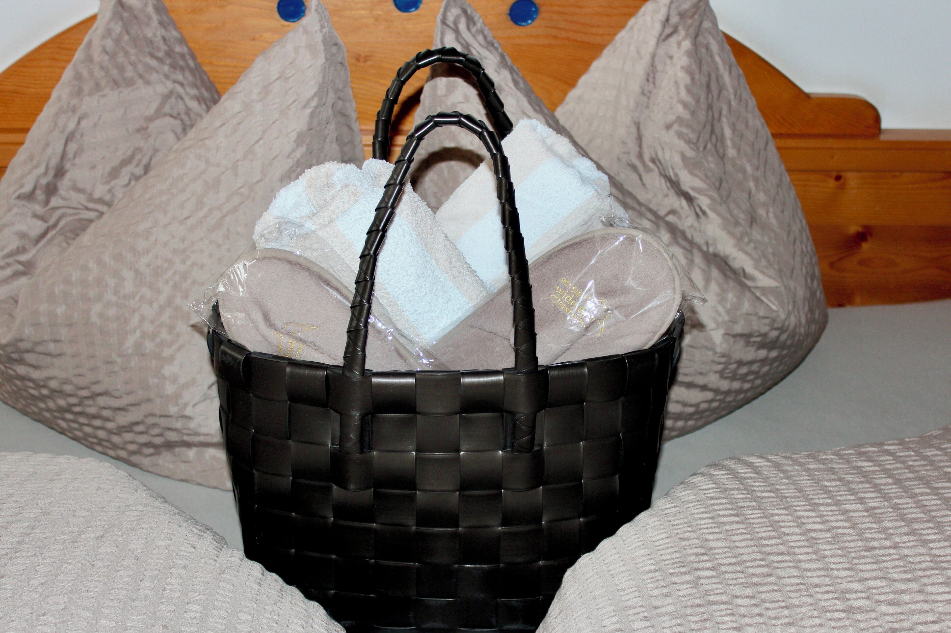 A black woven basket with handles containing white and beige pillows.