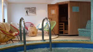 A swimming pool with metal ladders, surrounded by colorful wicker chairs, and a wooden sauna door. - Pension Widmann (Moso in Passiria)