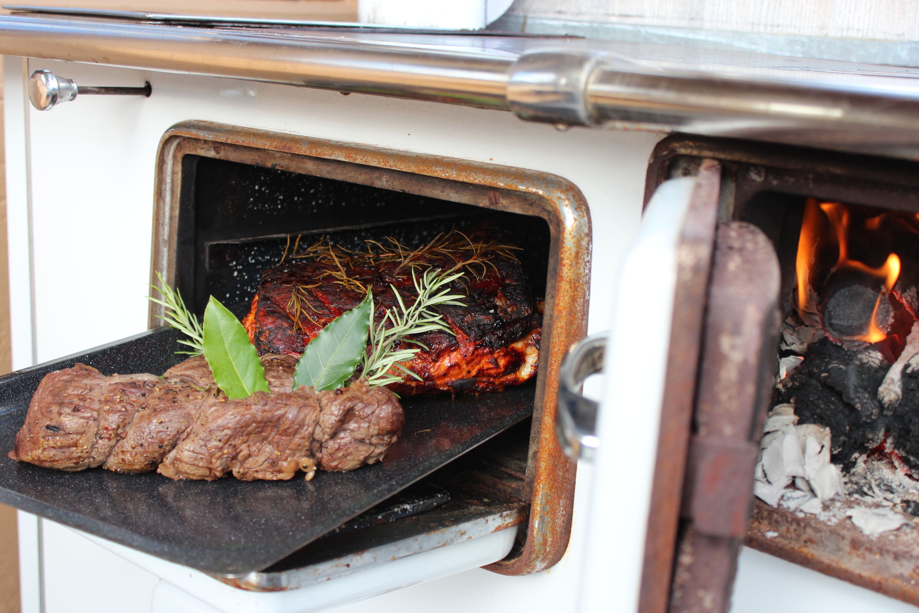 An open oven with meat and herbs inside.