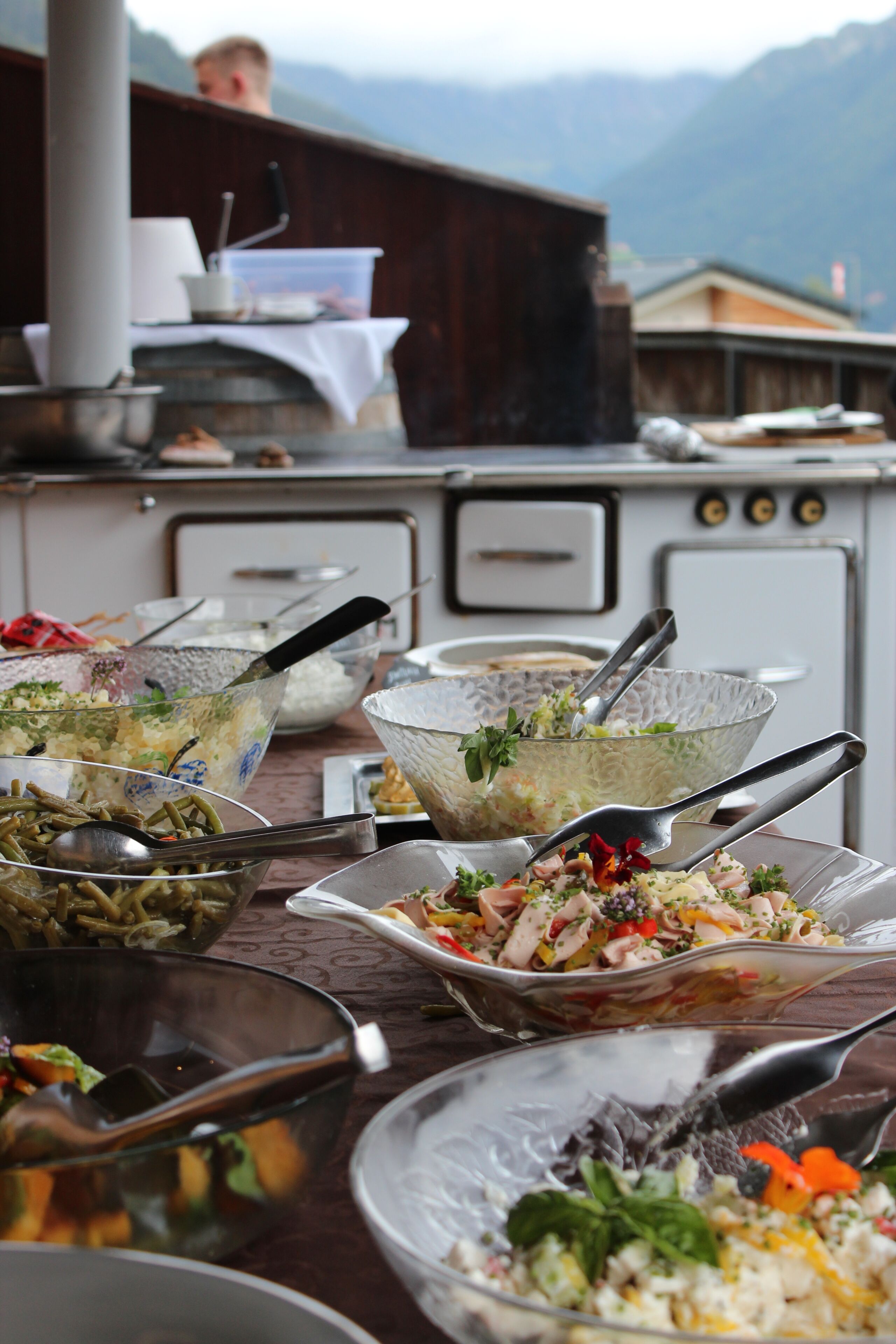 A dining table with various dishes and utensils, a wooden table, and a kitchen area with cabinets and appliances in the background.