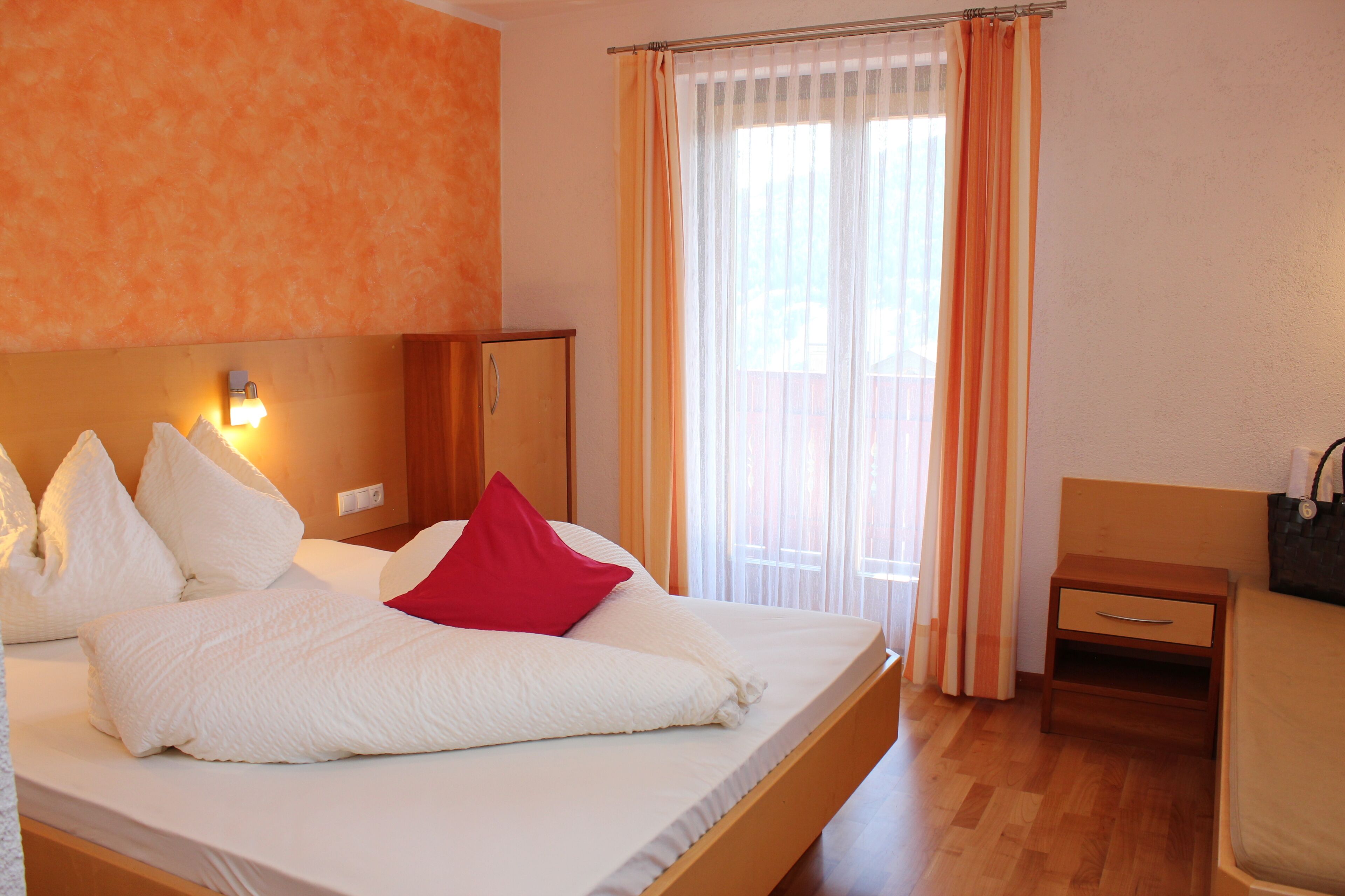 Habitación de hotel con cama, mesita de noche, cabecera de madera, lámpara de pared y ventana con cortinas.