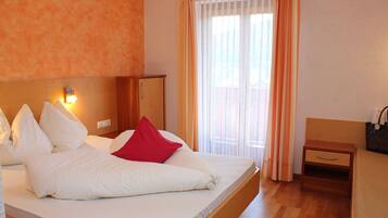 Habitación de hotel con cama, mesita de noche, cabecera de madera, lámpara de pared y ventana con cortinas.