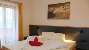 A bed with white bedding, a red pillow, and a mountain landscape painting above it. - Pension Widmann (Moso in Passiria)