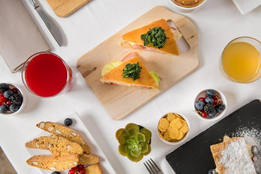 Desayuno con sándwich, fruta y una bebida sobre una mesa blanca.
