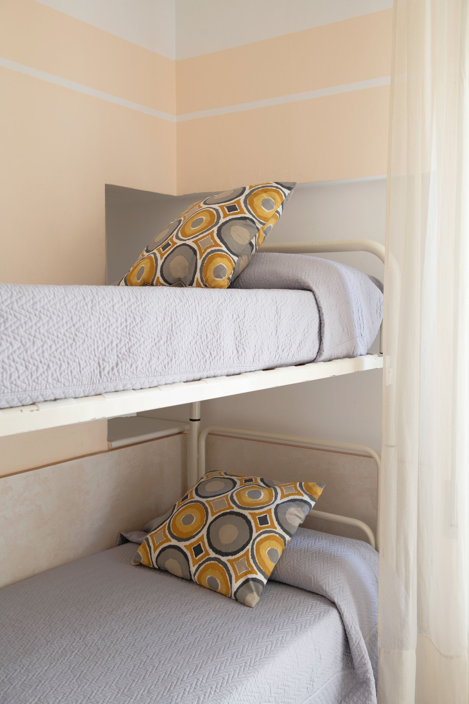 Una cama litera con almohadas estampadas y una manta con textura.