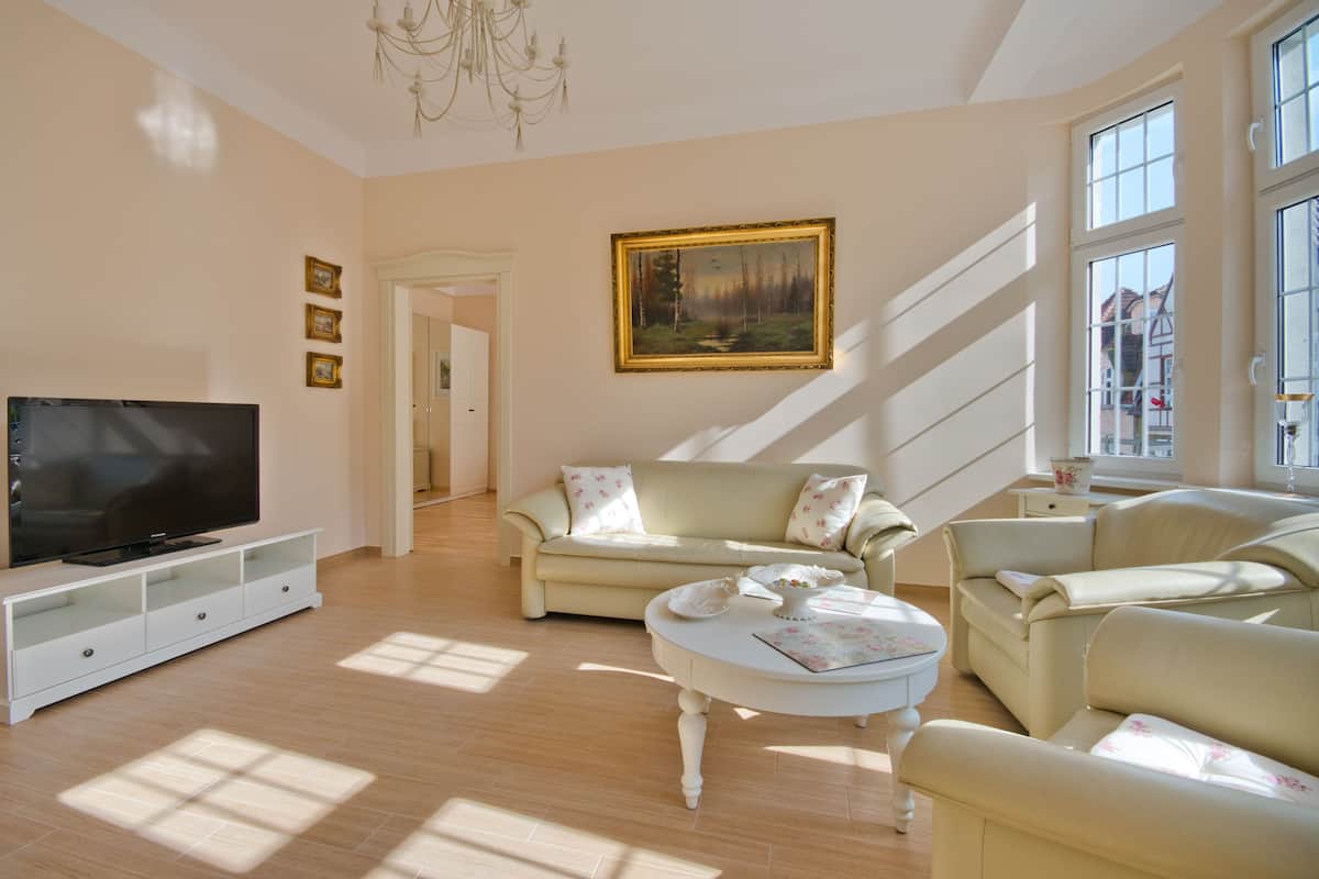 A spacious living room with a large flat-screen TV, two sofas, a coffee table, and a painting on the wall.