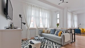 Una sala de estar moderna con un sofá gris, un reposapiés blanco y negro estampado y una alfombra geométrica.