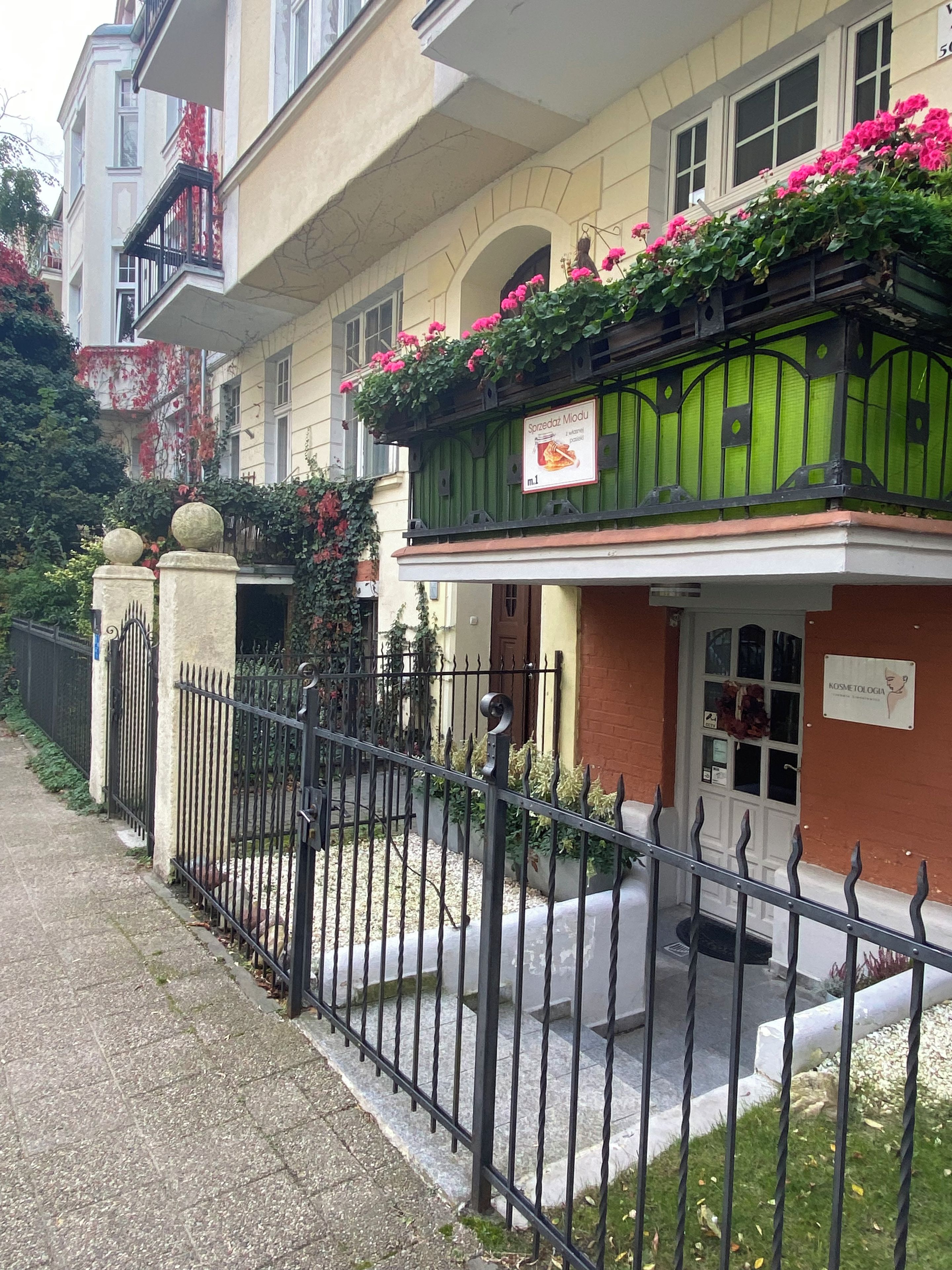 A building with a balcony adorned with flowers, a signboard, and a gated entrance.