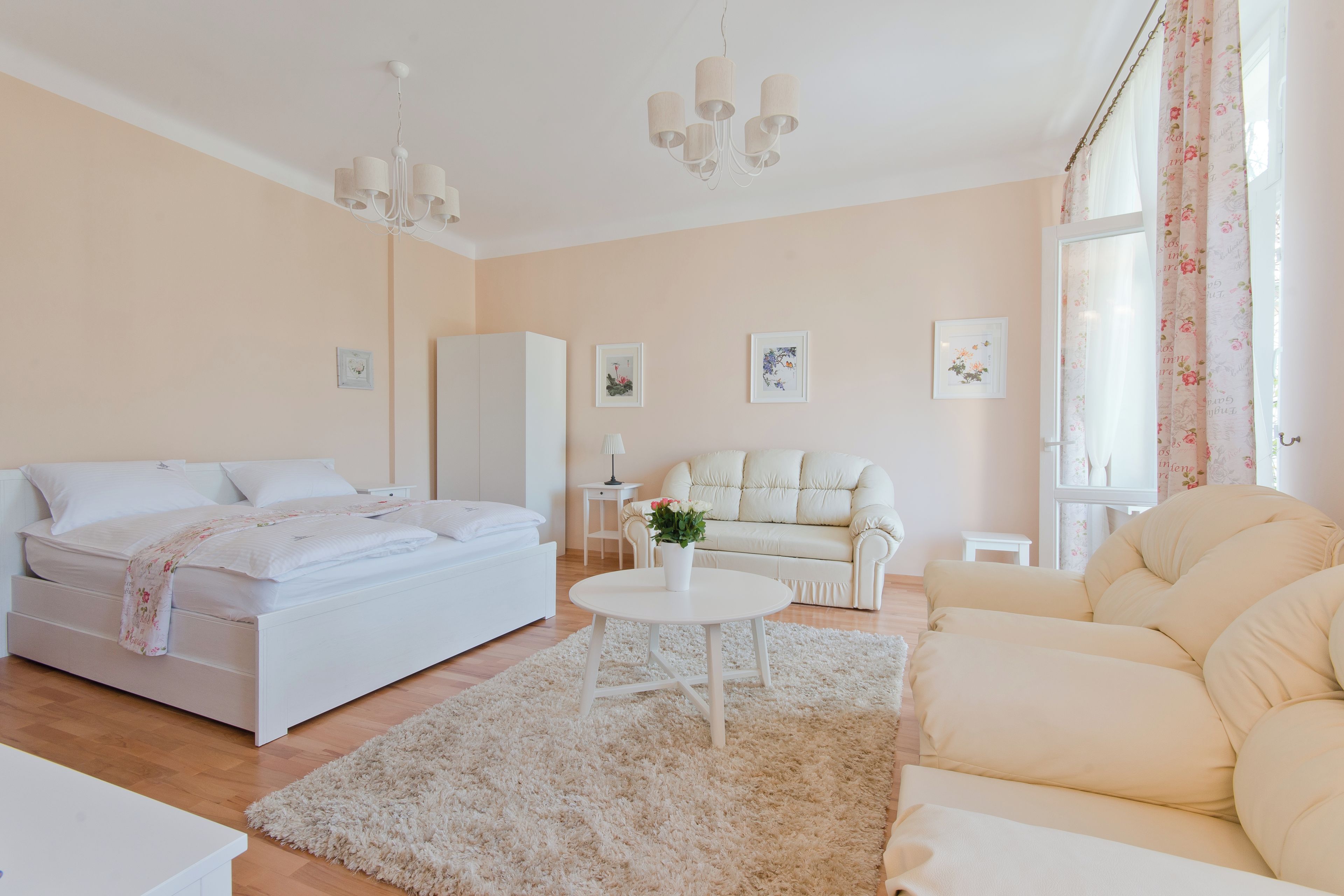 A bedroom with a bed, bedside tables, a nightstand, a sofa, a small table, and a window with curtains.