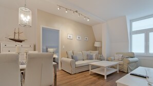 A modern living room with a sofa set, a dining table, and a chandelier.