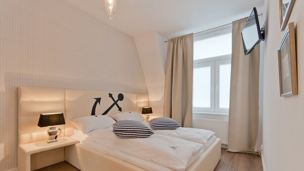 A bedroom with a large bed, bedside tables, a TV mounted on the wall, and a window with curtains.