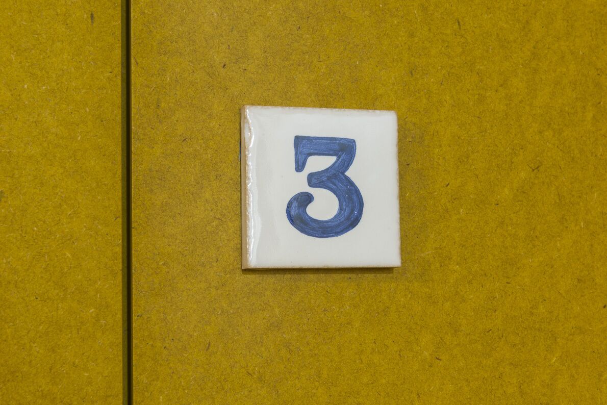 Eine weiße Fliese mit der Zahl 3 in Blau auf gelbem Grund.