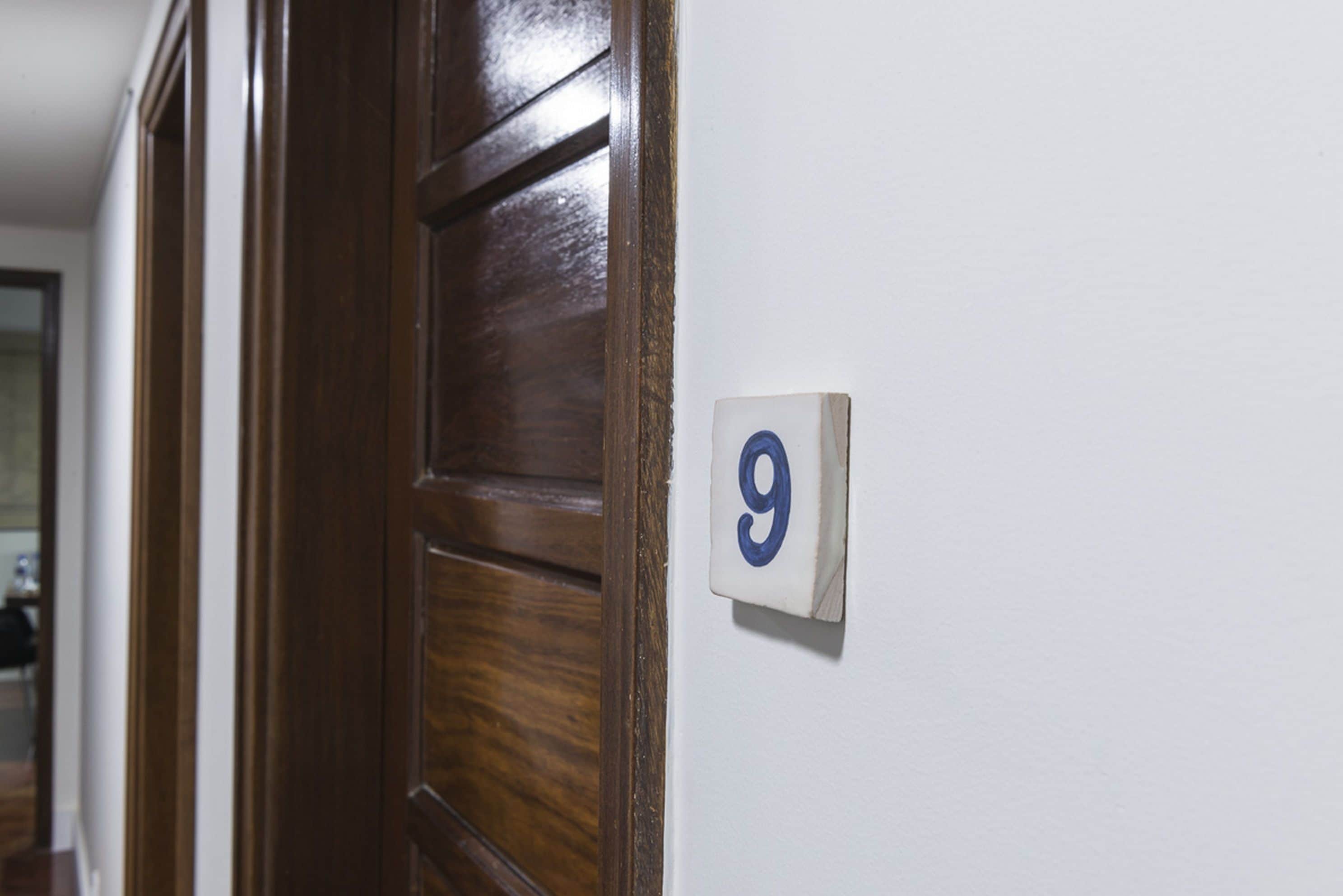Puerta de madera con pared blanca y un cartel con el número 9.
