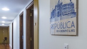 Un corridoio con pavimento in legno, un quadro appeso al muro e una porta con cornice dorata.