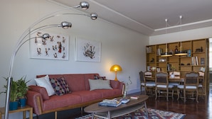 Un soggiorno con un divano rosso, un tavolino, un tappeto decorato, una libreria e una zona pranzo con sedie e un tavolo.