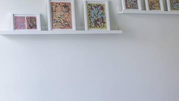 Quarto com cama, um banquinho e prateleira na parede com obras de arte emolduradas.