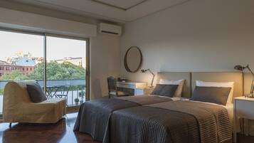 Habitación de hotel con dos camas, un escritorio, una silla y un ventanal grande con vista a la ciudad.